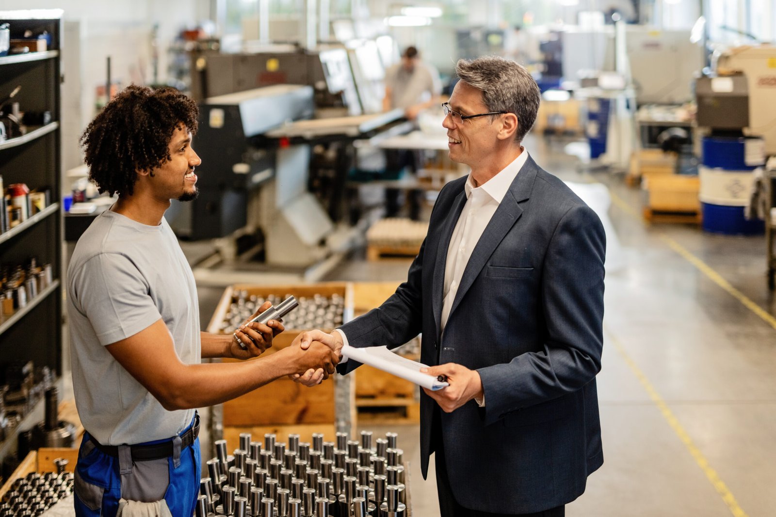Manager and technician shaking hands in a manufacturing facility with equipment background